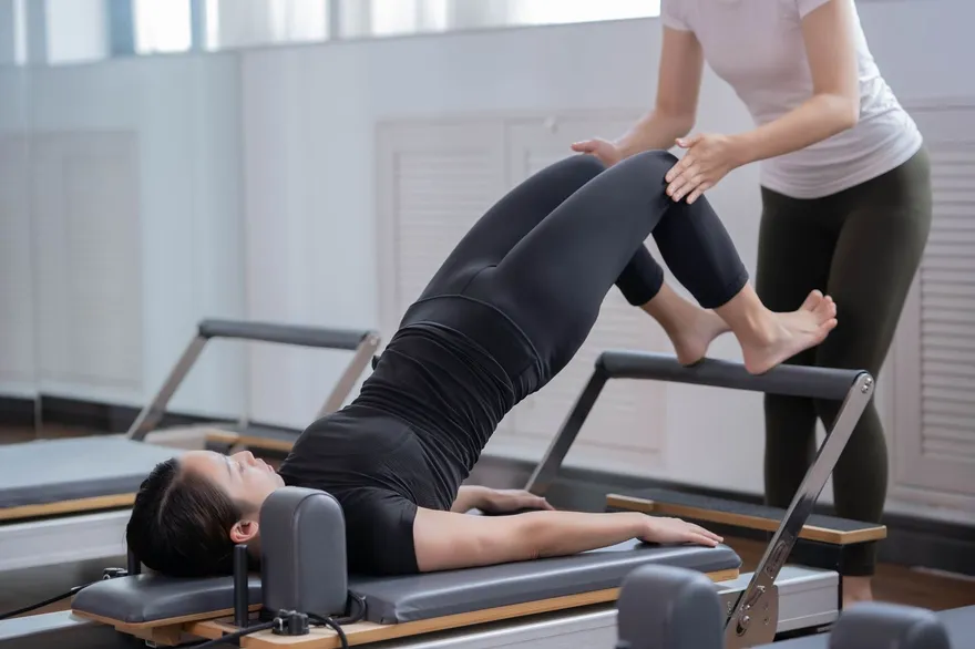 Profesora ajustando la postura de una alumna tumbada en el reformer